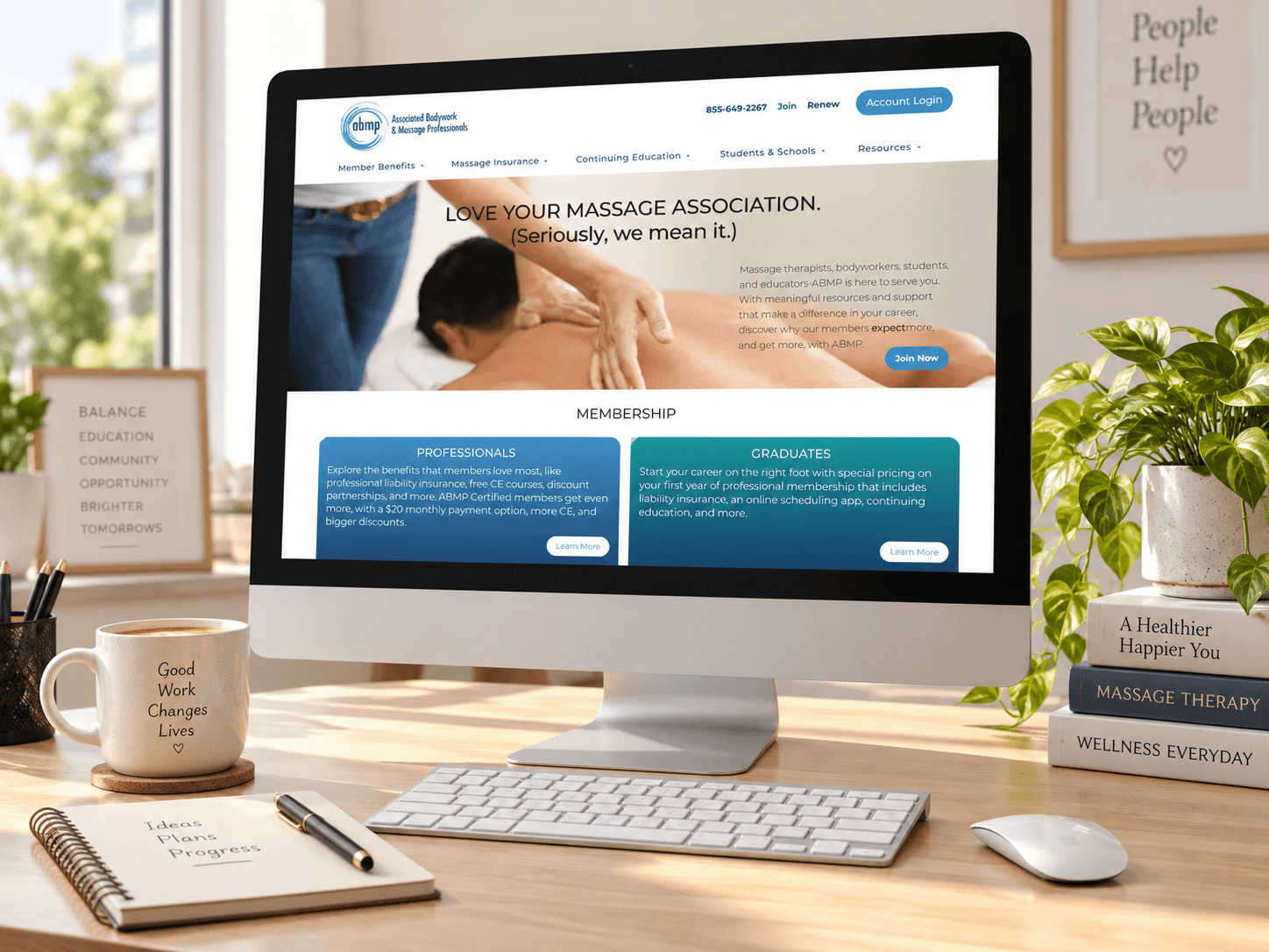 ABMP website displayed on iMac on wood grain desktop.